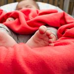 Adorable baby sleeping wrapped in a cozy red blanket, showing tiny feet.